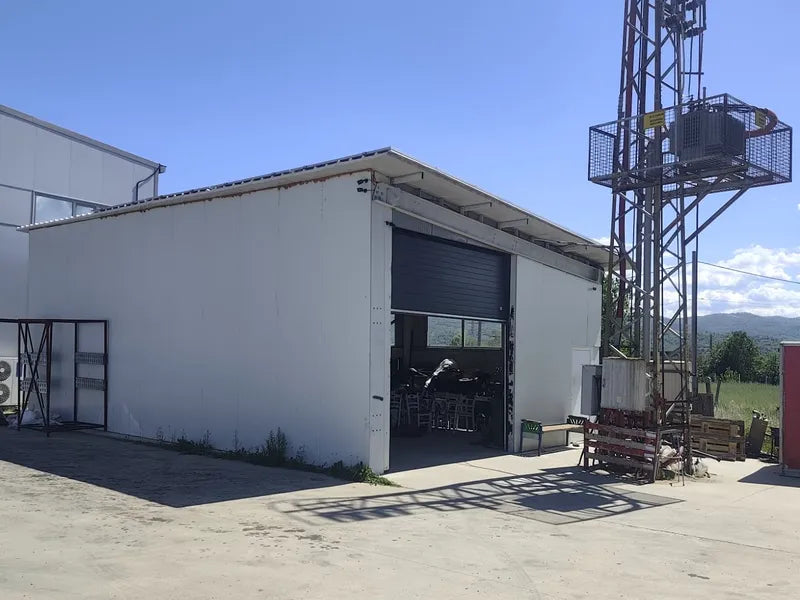 Сградата на монтажния център Garage46 в Благоевград - бяла сграда с гаражна врата и метална кула до нея